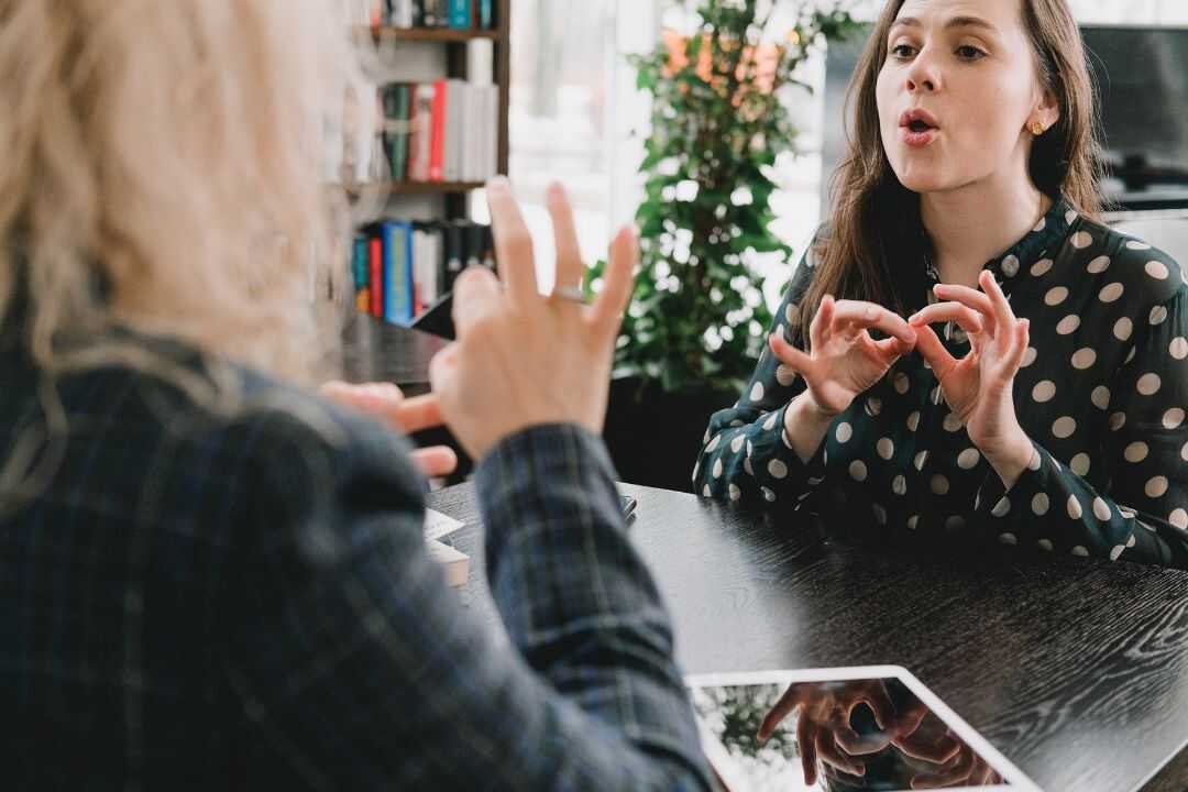 Two women engaged in a lively discussion at a work table, showcasing effective communication—a key focus of our team-building activities for HR professionals, aimed at enhancing collaborative skills.