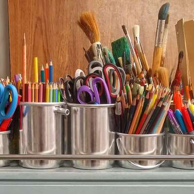 A colorful assortment of art supplies including pencils, pens, scissors, rulers, and brushes organized in metal containers, perfect for creative team-building activities booked by HR professionals.