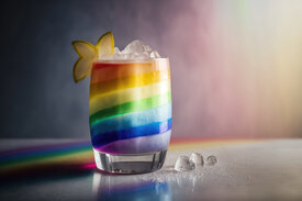 A vibrant cocktail glass layered with rainbow colors, garnished with a star fruit slice and ice cubes, symbolizing creative and refreshing team-building activities designed for HR professionals.