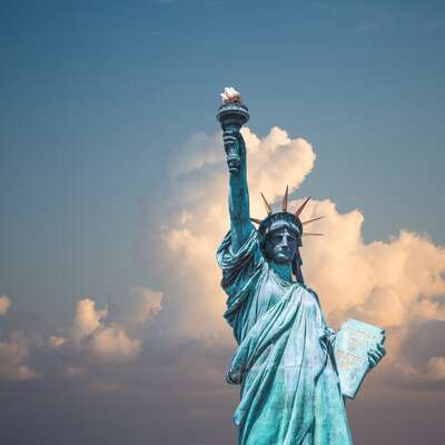 The Statue of Liberty against a backdrop of fluffy clouds and a clear blue sky, symbolizing freedom and unity. Perfect for HR professionals planning inspiring and culturally rich teambuilding activities.