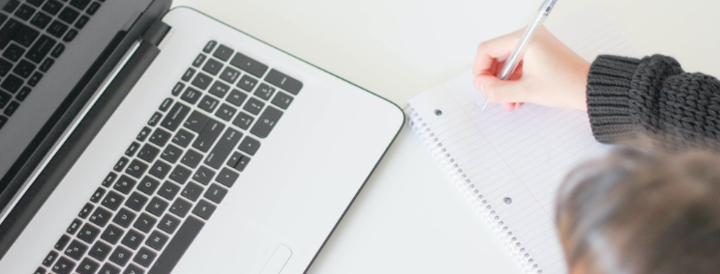 A person writing in a notebook next to a laptop, symbolizing planning and organization for team-building events tailored for HR professionals.