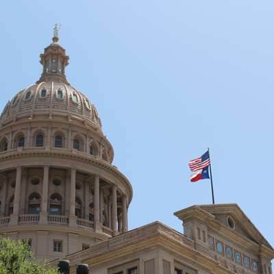 A scenic view of a historic domed building adorned with American and Texas flags. Ideal for corporate teambuilding events, this architectural landmark symbolizes unity and collaboration, perfect for HR professionals planning dynamic group activities.