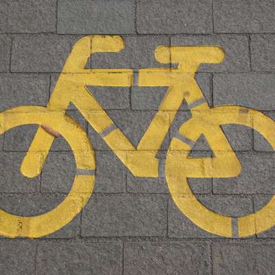 Yellow bicycle symbol painted on a gray cobblestone path, representing eco-friendly and active teambuilding activities for HR professionals to book, promoting health and collaboration.